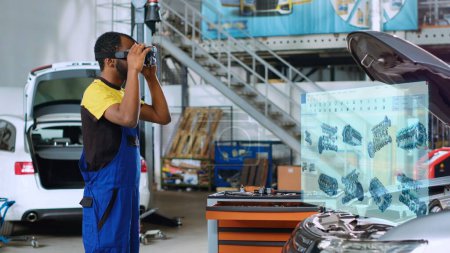 Photo for Mechanic in repair shop using advanced virtual reality technology software to visualize car engine parts in order to fix it. Garage worker wearing high tech vr goggles while mending broken vehicle - Royalty Free Image