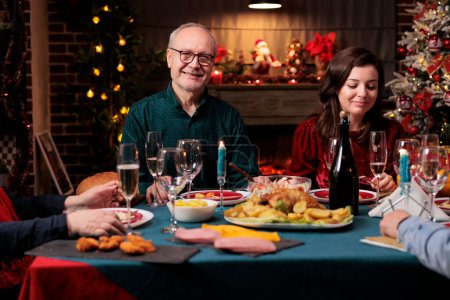Photo for Senior person at christmas dinner event with friends eating homemade food and enjoying xmas eve together at home. Men and women attending festive gathering during december winter season. - Royalty Free Image