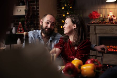 Photo for Sweet people meeting family at dinner on christmas eve, gathering around table with friends and relatives to eat traditional food and drink wine. Couple talking to persons during december event. - Royalty Free Image