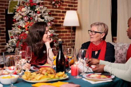 Photo for Jolly group of people enjoying xmas eve holiday at home, young and old family members having fun eating homemade food and drinking alcohol. Friends gathering around festive dinner table. - Royalty Free Image