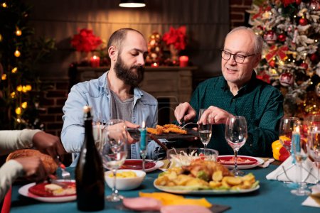 Téléchargez les photos : Diverses personnes se rassemblent autour de la table pour célébrer les vacances d'hiver festives, se sentant heureux pendant le dîner de la veille de Noël. Amis et famille appréciant le temps à la maison avec la nourriture traditionnelle maison. - en image libre de droit