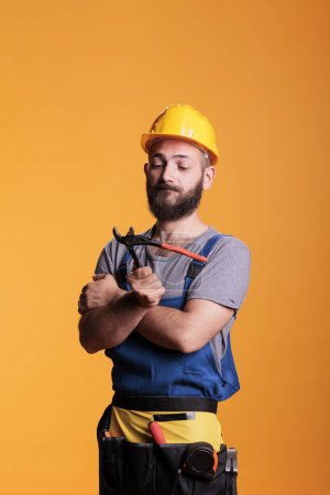 Photo for Professional repairman holding pair of pliers to work on house renovation, standing in studio. Construction worker foreman using pliers and refurbishment tools, industrial engineering. - Royalty Free Image