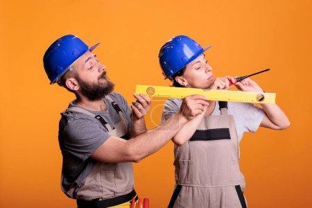 Photo for Contractors holding screwdriver and water level tool in studio shot, using ruler or leveler to work on renovation. Team of building experts being confident with renovating tools. - Royalty Free Image