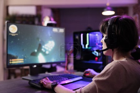 Photo for Professional gamer engaging in online competitive multiplayer tourney using cutting edge gaming system, captivating fans during live stream. Woman in rgb lights lit living room playing videogames - Royalty Free Image