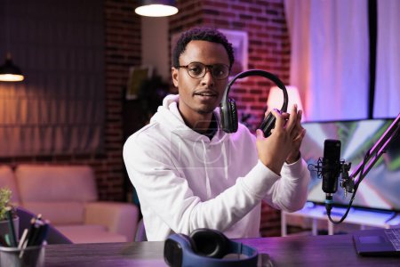 Photo for Portrait of african american tech vlogger reviewing headphones in living room studio. Entertaining content creator filming technology channel vlog for audiophiles, presenting info - Royalty Free Image