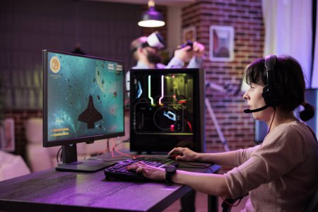 Photo for Gamer using professional grade level gaming setup to avoid disruptive lag while playing esports tournaments. Woman relaxing in rgb lights apartment playing action shooting videogame late at night - Royalty Free Image