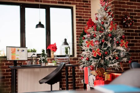 Foto de Espacio de trabajo de oficina decorado con árbol de navidad festivo y regalos durante la temporada de vacaciones de invierno. Cuadro de estadísticas del proyecto en la pantalla del ordenador en el lugar de trabajo durante la celebración del año nuevo - Imagen libre de derechos