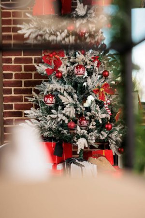 Photo for Artificial christmas tree decorated with red baubles behind window in brick wall office. Festive evergreen with ornaments during new year winter holiday season in corporate workplace - Royalty Free Image