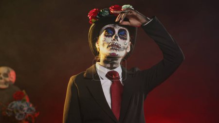 Photo for Spooky goddess in halloween costume with skull make up celebrating holy mexican tradition, posing in studio. Looking like lady of death at santa muerte ritual celebration. Handheld shot. - Royalty Free Image