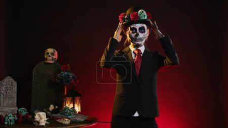 Photo for Cavalera catrina with suit and hat looking mysterious wearing festival skull body art, santa muerte celebrating dios de los muertos in studio. Woman looking like holy mexican entity. - Royalty Free Image