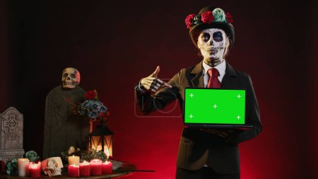 Photo for Mexican lady of death showing greenscreen template on laptop, smiling on dios de los muertos. Beautiful woman holding pc with isolated mockup display, chroma key and blank copyspace. - Royalty Free Image