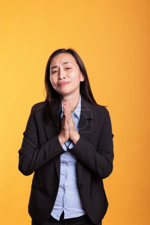 Téléchargez les photos : Femme asiatique debout avec les mains dans le geste de prière, étant religieuse en studio sur fond jaune. Adulte spirituel demandant pardon à Dieu, exprimant gratitude et croyance. Concept de religion - en image libre de droit