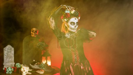 Photo for Beautiful woman with sugar skull body art and crown of flowers, dressed in costume of death as santa muerte. Dios de los muertos halloween art to celebrate holy mexican tradition in studio. - Royalty Free Image