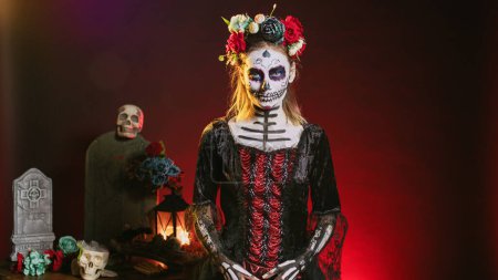 Photo for Spooky goddess of death with skull make up and horror costume to celebrate dios de los muertos on mexican halloween. Creepy woman dressed as santa muerte on day of the dead holiday. - Royalty Free Image