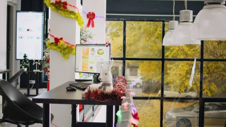 Téléchargez les photos : Espace de travail moderne décoré élégant et festif avec un arbre de Noël joliment décoré. Cartes d'affaires sur écran d'ordinateur à Noël ornent lieu de travail pendant la saison des vacances d'hiver - en image libre de droit