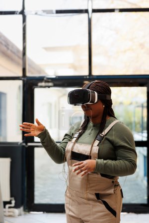 Photo for Supervisor checking clients online orders using virtual reality headset before start preparing packages in storage room. African american manager wearing industrial overall during goods inventory - Royalty Free Image