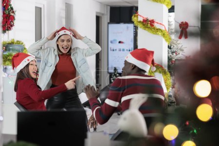 Photo for Coworkers having fun in festive decorated office, making fun of each other at work during winter holiday season. Employees laughing together in Christmas ornate workspace - Royalty Free Image