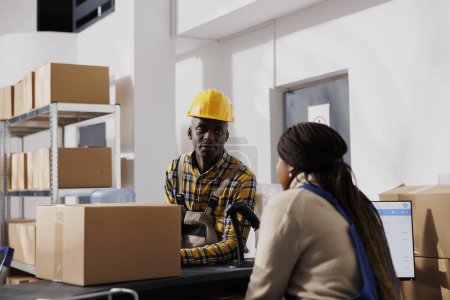 Photo for Warehouse worker putting parcel on counter desk for dispatching. African american retail storehouse employees managing customer order packing and delivery in storage room - Royalty Free Image