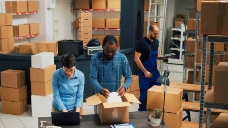 Foto de Employees putting products in boxes and dong highfive, celebrating stock shipment and delivery. Team of people working on retail development, shipping merchandise in packages. - Imagen libre de derechos