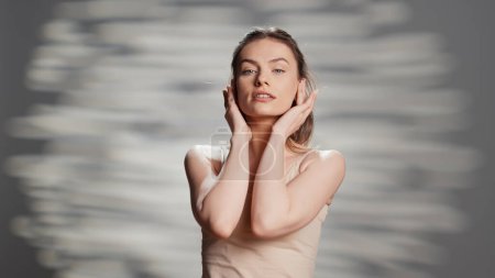 Photo for Positive gentle woman applying face cream for ad, creating beauty routine campaign with moisturizer and nourishing products. Sensual luminous girl with radiant bare skin promoting self love. - Royalty Free Image