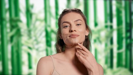 Téléchargez les photos : Luminous radiant woman posing with confidence, creating self love skincare ad campaign in studio. Beautiful smiling girl feeling happy over bamboo trees background, self acceptance. - en image libre de droit