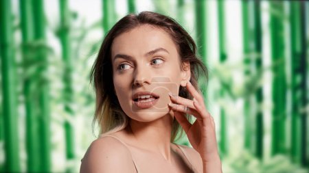 Foto de Caucasian woman embracing imperfections over bamboo background, promoting shampoo and conditioner on camera. Young flawless model advertising hair care and beauty routine in studio. - Imagen libre de derechos