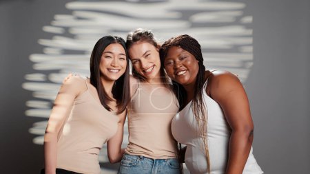 Téléchargez les photos : Diverse friends acting cheerful about body acceptance in studio, feeling beautiful and advertising skincare campaign. Young glamorous women smiling on camera and promoting body positivity. - en image libre de droit