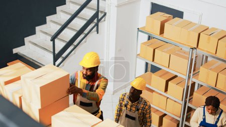 Photo for Warehouse workers organizing goods in packs, putting boxes in racks and shelves at job. Team of people taking boxes of products in storage room, working with containers. Handheld shot. - Royalty Free Image