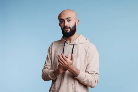 Photo for Arab man applauding with hands while standing and looking at camera with neutral expression. Young bald bearded person clapping with arms, congratulating and supporting studio portrait - Royalty Free Image