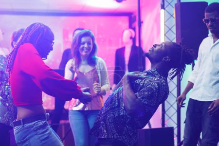 Couple improvising dance battle while clubbing and partying in nightclub. African american man and woman showing moves on dancefloor while having fun at discotheque social gathering