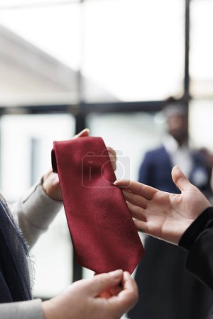 Téléchargez les photos : Client âgé tenant une cravate rouge analysant le matériel dans le centre de vêtements, magasinant pour des vêtements formels et des accessoires élégants. Employé de magasin aidant la femme à choisir la marchandise. Concept de mode - en image libre de droit