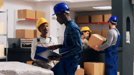 Photo for African american people doing quality control in warehouse, working with merchandise from depot shelves. Team of man and woman checking products for industrial service. Handheld shot. - Royalty Free Image
