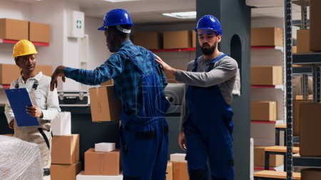 Photo for Multiethnic group of employees working with products in packages, planning shipment for goods distribution. Men and women looking at cardboard boxes filled with merchandise. Tripod shot. - Royalty Free Image