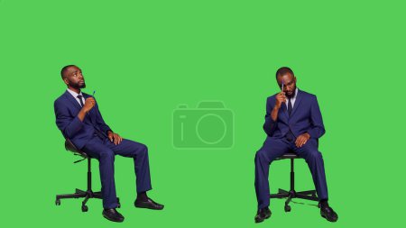 Téléchargez les photos : Un employé pensif réfléchissant à des solutions assis sur une chaise, posant sur un écran vert portant un costume de bureau d'affaires. Homme entrepreneur remue-méninges de nouvelles idées et se sentir confiant. - en image libre de droit