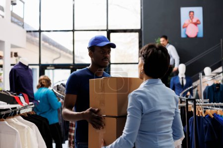 Photo for African american courier holding cardboard boxes, discussing shipping detalis with woman manager in shopping centre. Man in delivery uniform working with fashion store. Stylish boutique concept - Royalty Free Image