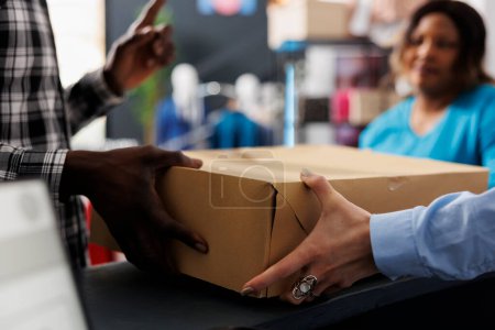 Foto de Hombre Shopaholic sosteniendo la caja de cartón en el mostrador, después de comprar mercancía de moda. Hombre afroamericano comprando ropa elegante, discutiendo sobre el material en la boutique moderna - Imagen libre de derechos