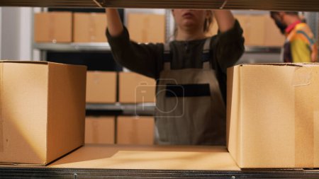 Photo for Female worker moving packs of goods, preparing order shipment for retail store business in storage room. Employee sorting boxes on racks in warehouse, supply chain and production. Tripod shot. - Royalty Free Image