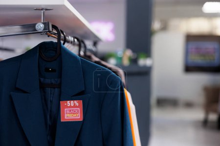 Photo for Close up of classic formal jacket with red Black Friday price tag hanging on cloth rack in empty modern fashion store. Special offers in clothing store during seasonal discount sales - Royalty Free Image