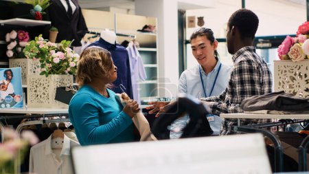 Foto de Clientes afroamericanos pidiendo ayuda a los empleados, explicando la tela de la ropa durante la sesión de compras en la boutique moderna. Pareja alegre de compras de mercancía de moda en la tienda de ropa - Imagen libre de derechos