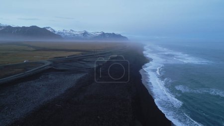Foto de Drone tiro de playa de arena negra nórdica en iceland, paisaje de costa oceánica polar con montañas nevadas. Hermoso paisaje icelandés con vista panorámica sobre la orilla atlántica. Movimiento lento. - Imagen libre de derechos