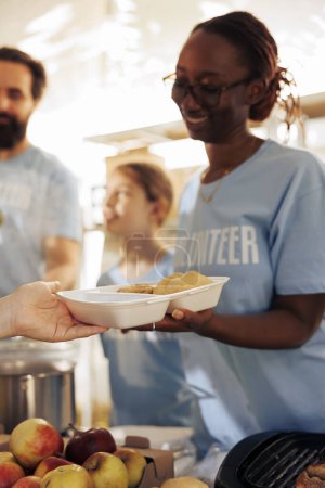 Foto de Una imagen detallada muestra a voluntarios que proveen comida gratis a los hambrientos, sin hogar y refugiados. Acercamiento de las mujeres voluntarias que distribuyen comidas, prestan asistencia y comparten alimentos no perecederos. - Imagen libre de derechos