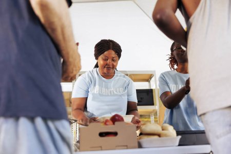 Foto de Mujeres voluntarias afroamericanas en organizaciones benéficas que brindan asistencia a los necesitados repartiendo comida gratis. Trabajadores de la caridad que contribuyen al programa de alivio del hambre ayudando a los menos privilegiados. - Imagen libre de derechos