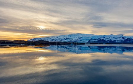 Photo for Lake and snowy mountains at sunset in iceland with majestic nordic landscape, freezing cold water. Scandinavian roadside scenery with hills during golden hour, wonderland scenic route. - Royalty Free Image