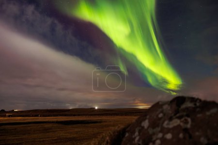 Foto de Luces boreales y montañas cubiertas de nieve en Islandia. Aurora boreal formando un hermoso paisaje bajo el cielo estrellado nocturno. Colorido fenómeno mágico brillante con colinas nevadas y rocas. - Imagen libre de derechos