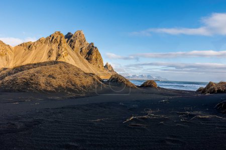 Foto de Colinas de Vestrahorn en la península norte, con una playa de arena negra única y un idílico telón de fondo polar. Increíble paisaje creado por las laderas rocosas y la costa del océano, olas altas. - Imagen libre de derechos