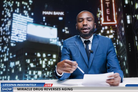 Photo for TV reporter discusses about anti aging drug discovered by medical scientists, miraculous experiment to preserve youth and stop growing old. African american newscaster on night show. - Royalty Free Image
