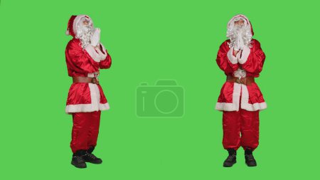 Photo for Saint nick holds hands in a prayer standing on full body greenscreen backdrop, acting spiritual in studio. Santa claus embodiment talking to jesus, spreading positive christmas eve spirit. - Royalty Free Image