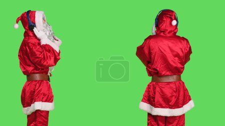 Photo for Dancer saint nick listen to music, having fun with headset against greenscreen background. Cool man portraying santa claus in suit with white beard dancing on songs, festive holiday event. - Royalty Free Image