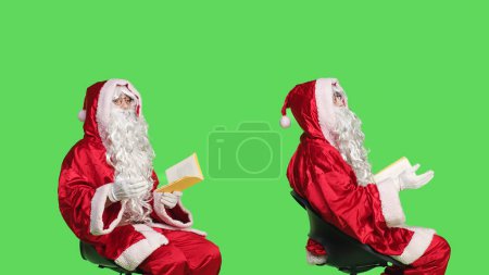 Photo for Saint nick reads poetry book in studio against isolated greenscreen backdrop, enjoying lecture of fairytale fiction or novel. Wise man reading literature for education, santa claus character. - Royalty Free Image