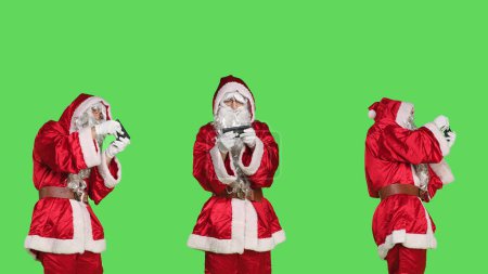 Foto de Santa Claus juega videojuegos en el teléfono, divirtiéndose con la competencia de juegos móviles en línea. Persona que retrata la Navidad del padre en traje rojo sobre pantalla verde, entretenimiento y ocio. - Imagen libre de derechos